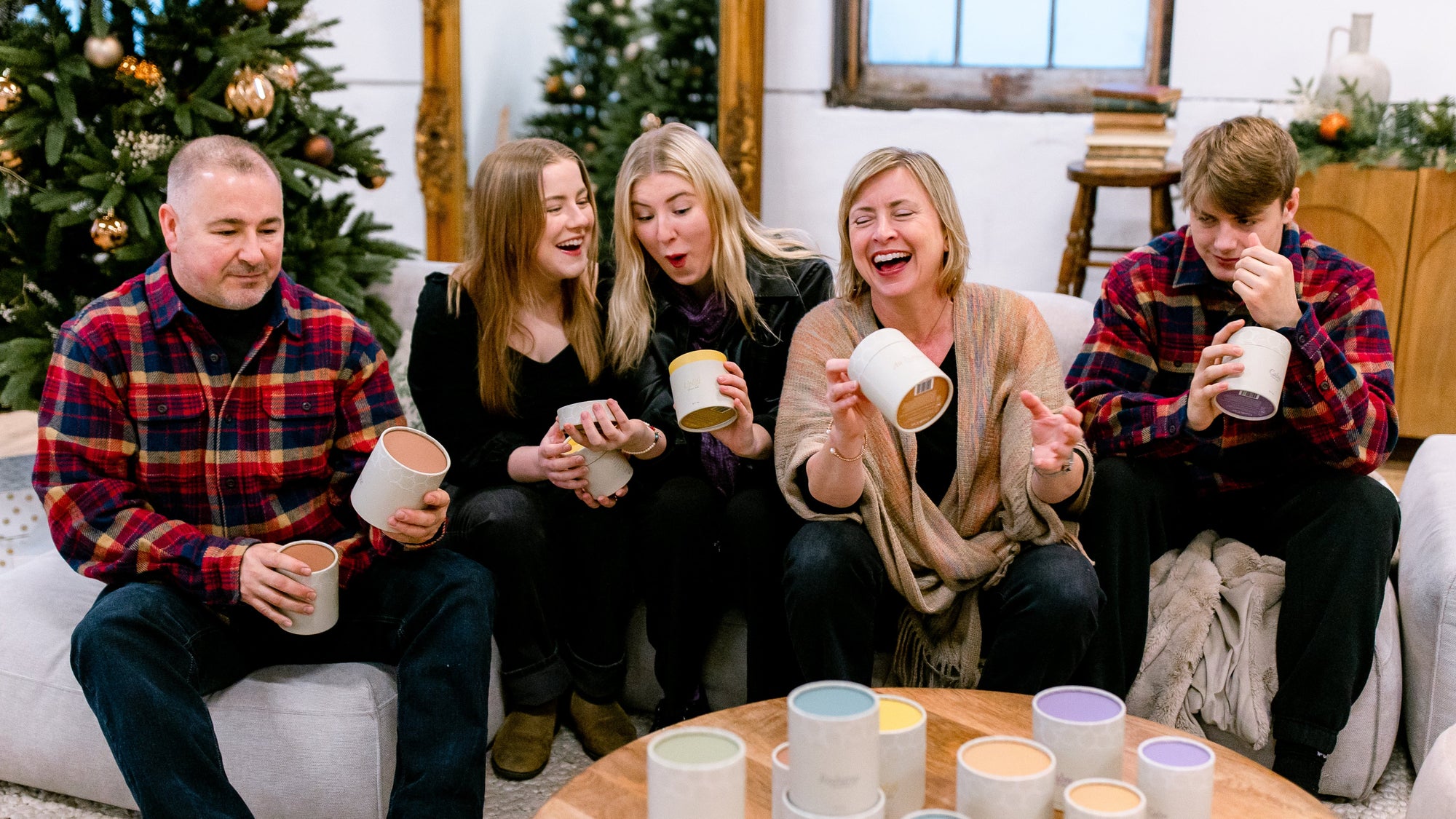 Green Ash's Owner with her family sitting on a couch, with the Green Ash candles in kraft tubes on the table. Each family member is holding 1 or 2 candles each, smiling and laughing