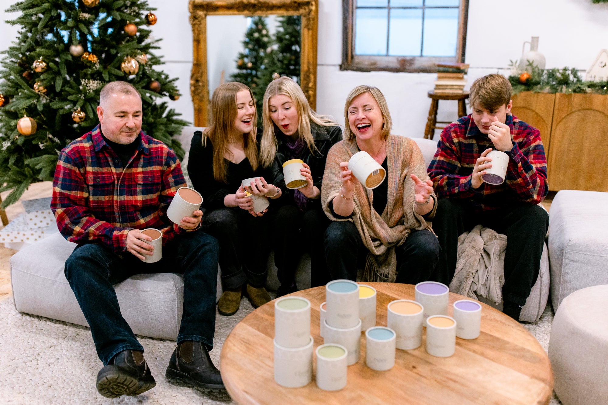 Green Ash's Owner with her family sitting on a couch, with the Green Ash candles in kraft tubes on the table. Each family member is holding 1 or 2 candles each, smiling and laughing
