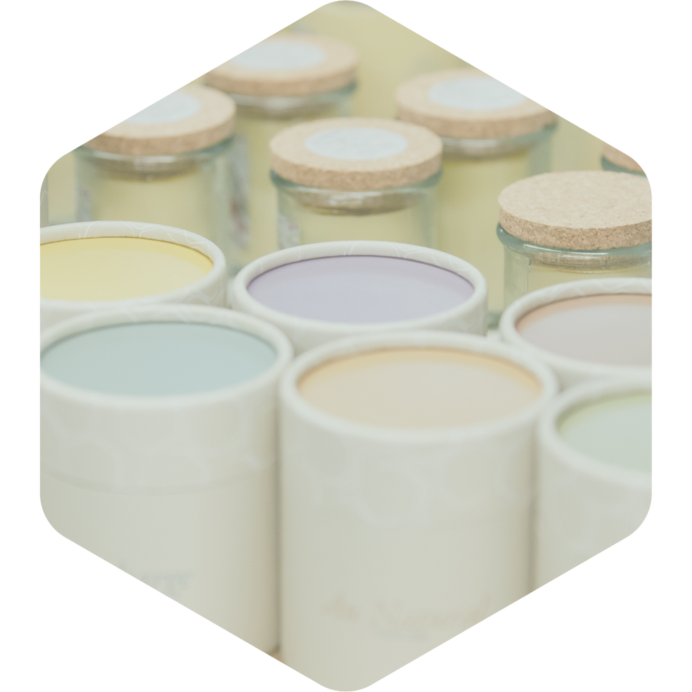 Close up image of Green Ash candles in their kraft tube packaging in the foreground, and jars are in the background.